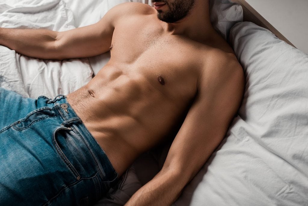 cropped man lying down on a bed focusing on his abs