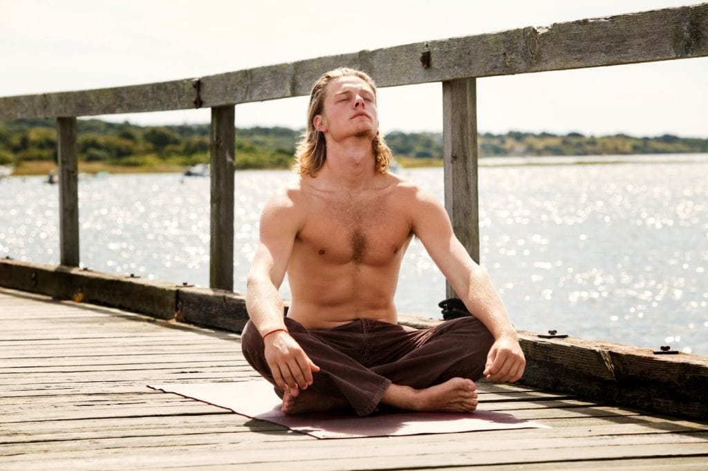 man meditating on a wooden bridge by the lake