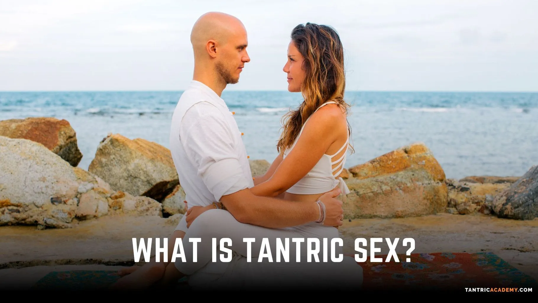 A couple sitting together on rocks by the sea, captioned what is tantric sex